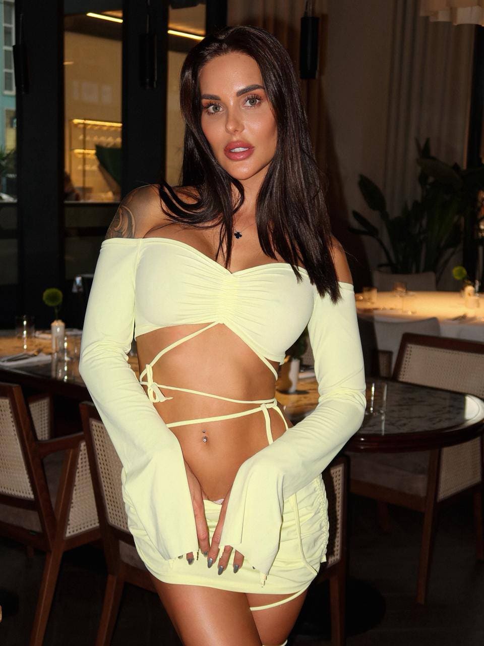 In a restaurant, she wears a pale yellow off-the-shoulder top with detached sleeves and a matching mini skirt.